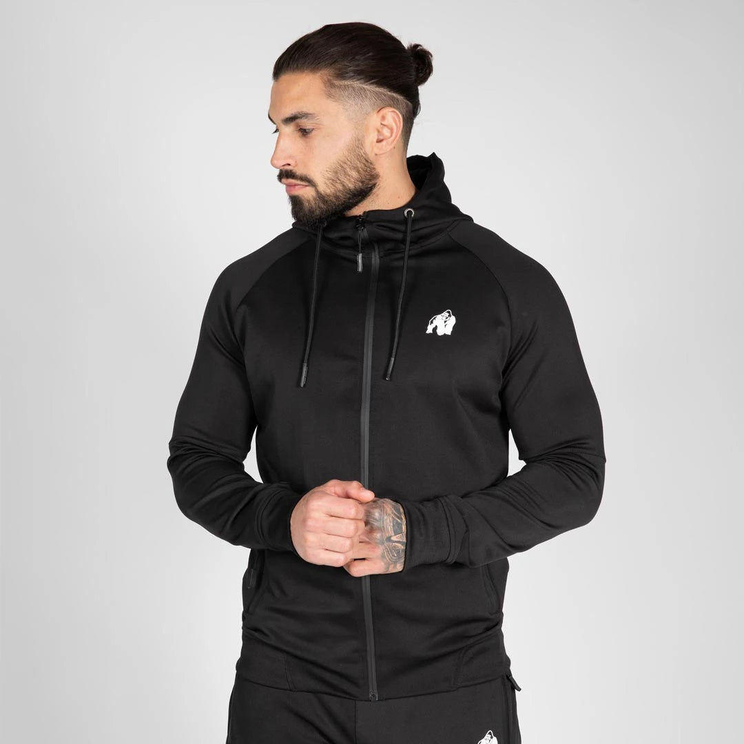Gorilla Wear Sullivan Track Jacket Black, musta urheilullinen treenitakki hupulla ja valkoisella logolla mallin yllä., kuva 5/7