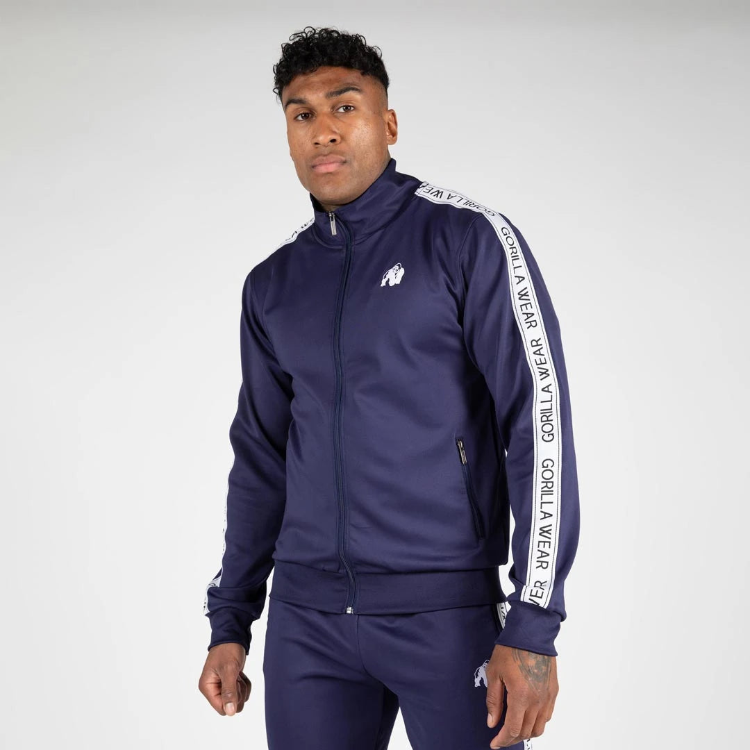 Mies yllään laivastonsininen Gorilla Wear Delaware Track Jacket navy, sporttinen treenitakki valkoisilla sivuraidoilla.