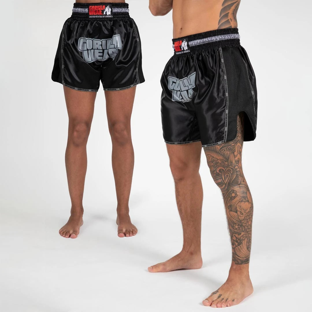 Gorilla Wear Piru Muay Thai Shorts black -kiiltävät shortsit isolla harmaalla logolla ja sivuhalkioilla.