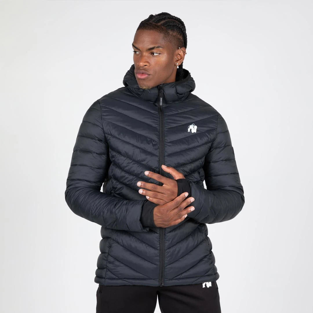 Mies yllään musta, topattu slim fit -mallinen Gorilla Wear Osborn Puffer Jacket Black -takki hupulla ja peukalonrei'illä.
