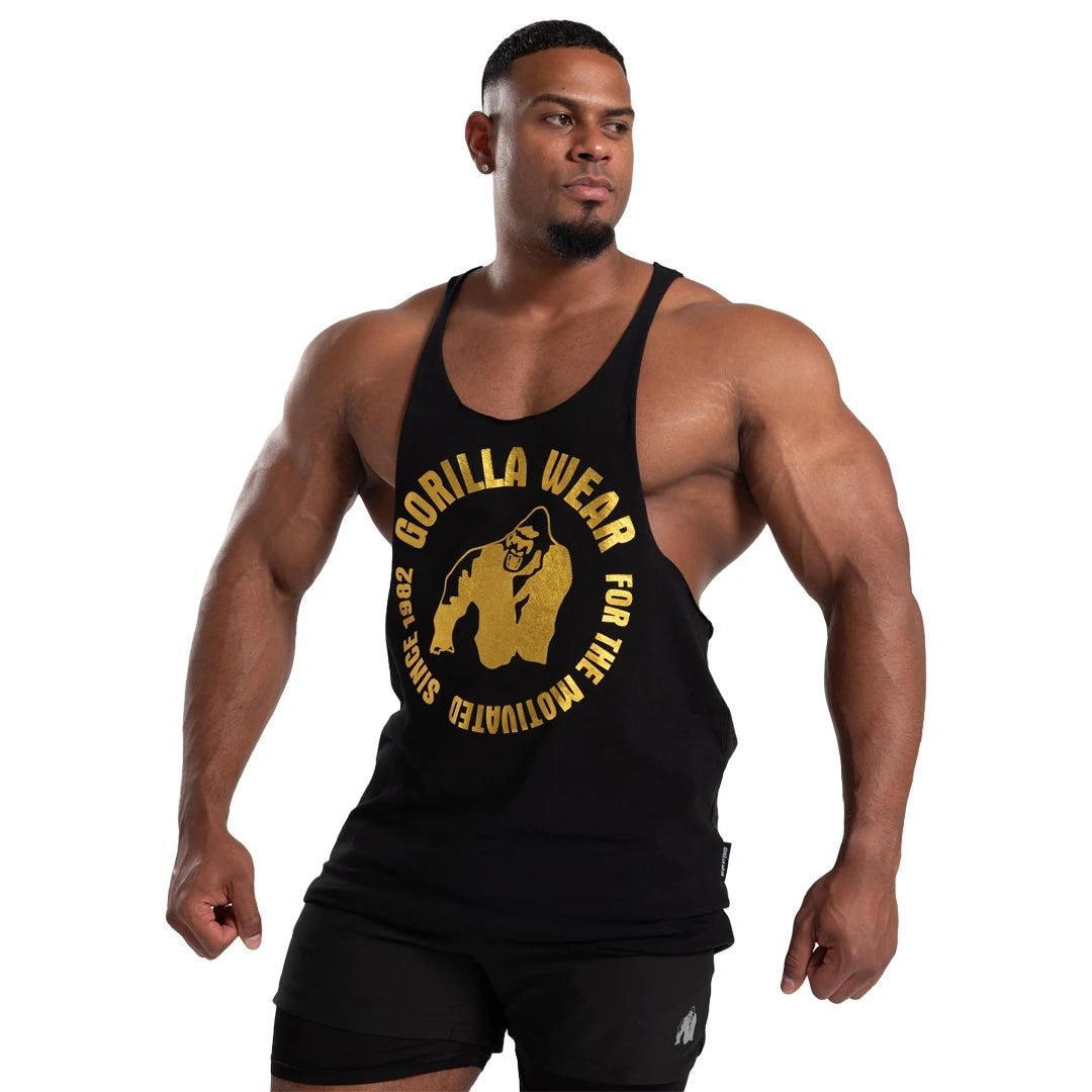 Gorilla Wear Melrose Stringer Black Gold, musta treenitoppi isolla kultapainatuksella lihaksikkaan miehen yllä.