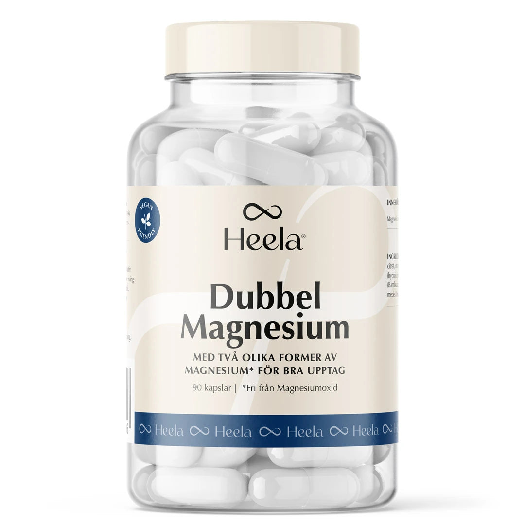 Heela Dubbel Magnesium 90 caps -ravintolisä läpinäkyvässä purkissa vaalealla etiketillä, täynnä valkoisia kapseleita.