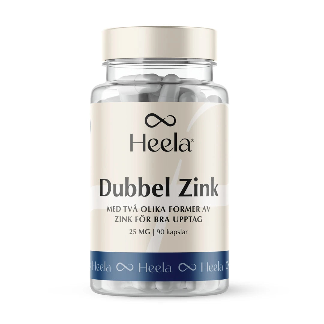 Heela Dubbel Zink 60 caps läpinäkyvässä purkissa, jossa on valkoisia kapseleita, beige etiketti ja sininen alaraita.