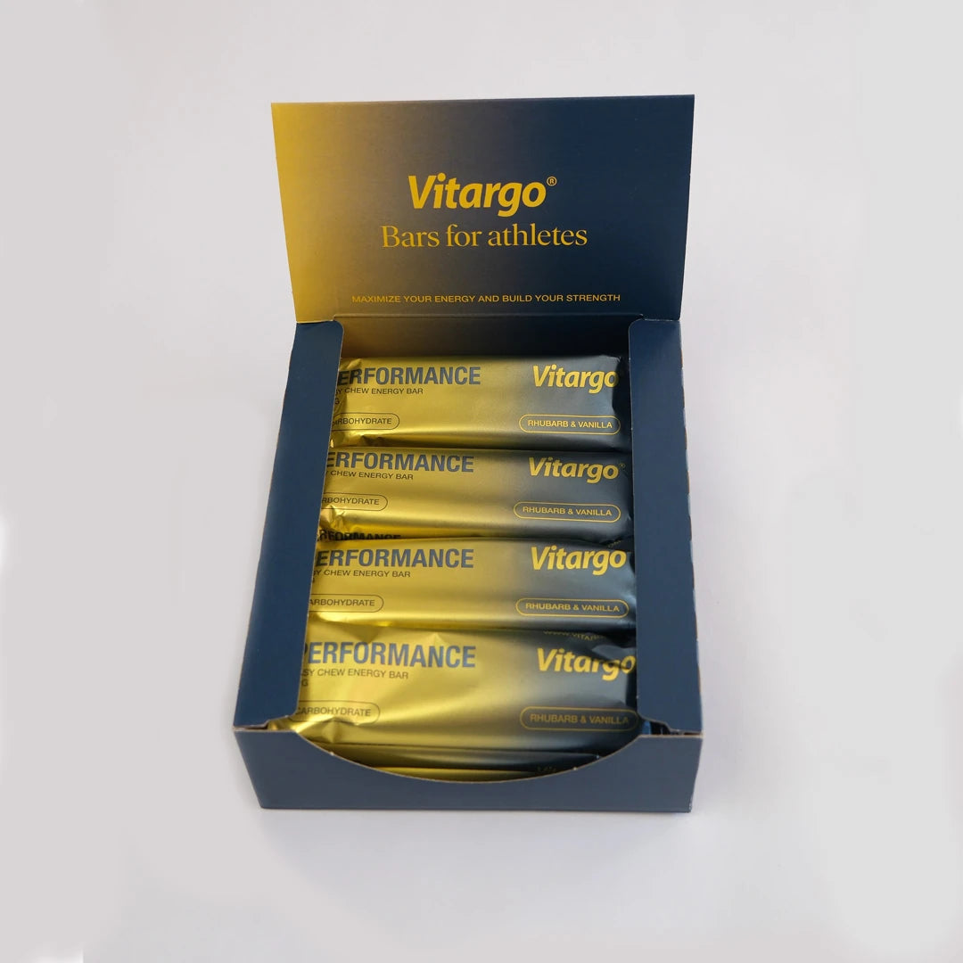 12 x Vitargo Performance Bar 55 g tummansinisessä laatikossa kultaisilla energiapatukoilla, makuna Rhubarb & Vanilla.