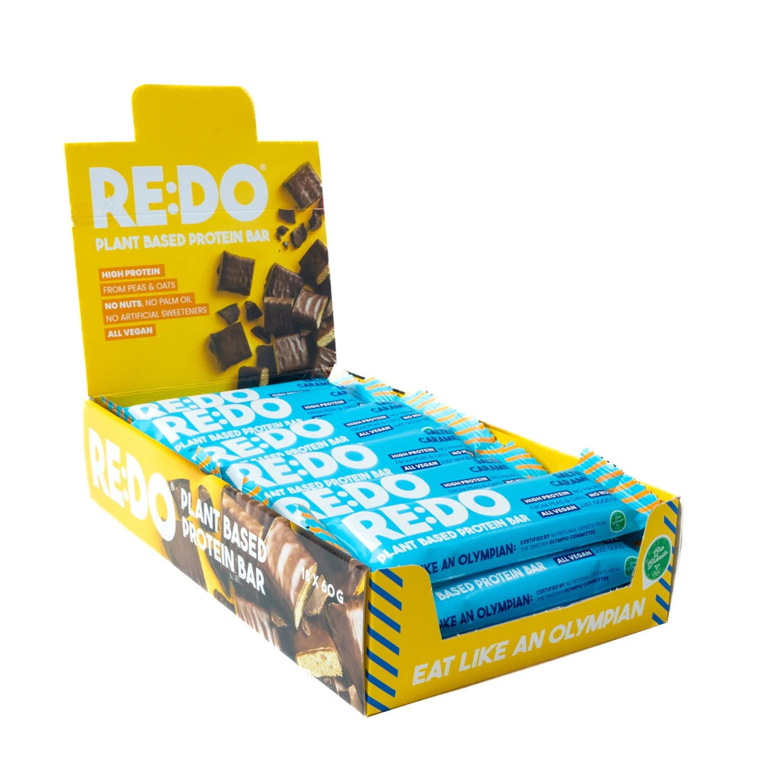 18 x REDO Bar 60 g Salty Caramel -proteiinipatukoita sinisissä kääreissä keltaisessa esittelylaatikossa.